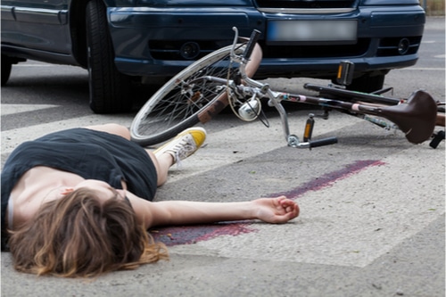 Woman lying next to her bike, car in the background