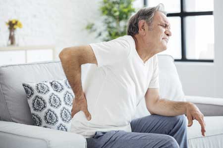 man sitting on couch holding back in pain