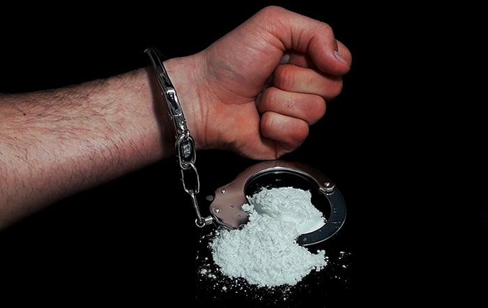 Handcuffed hand next to pile of cocaine
