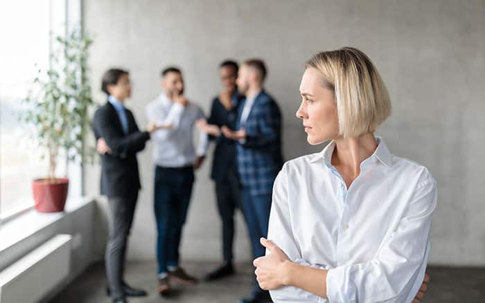 Male coworkers whispering behind back of female employee