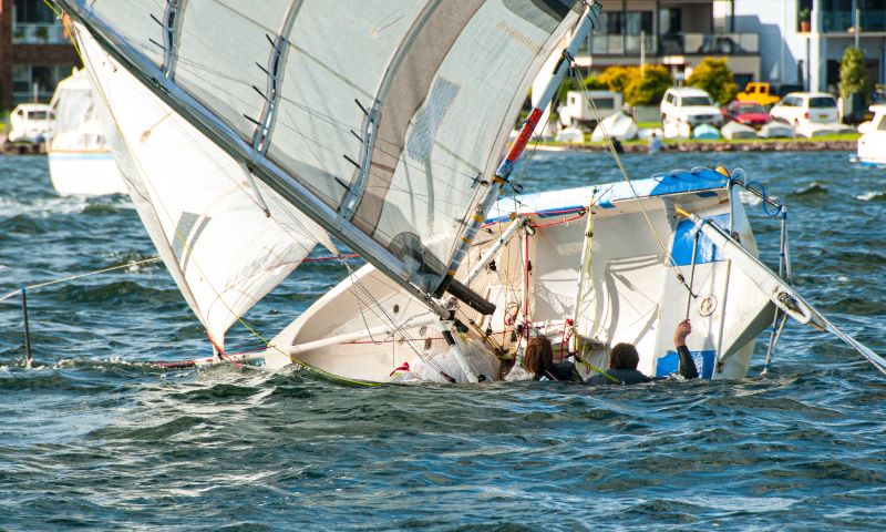 Two people in the water while their sailboat sinks