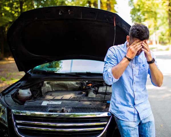 frustrated person in from of a broken down car with the hood up