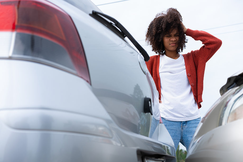 Young driver inspecting vehicle damage after accident she caused