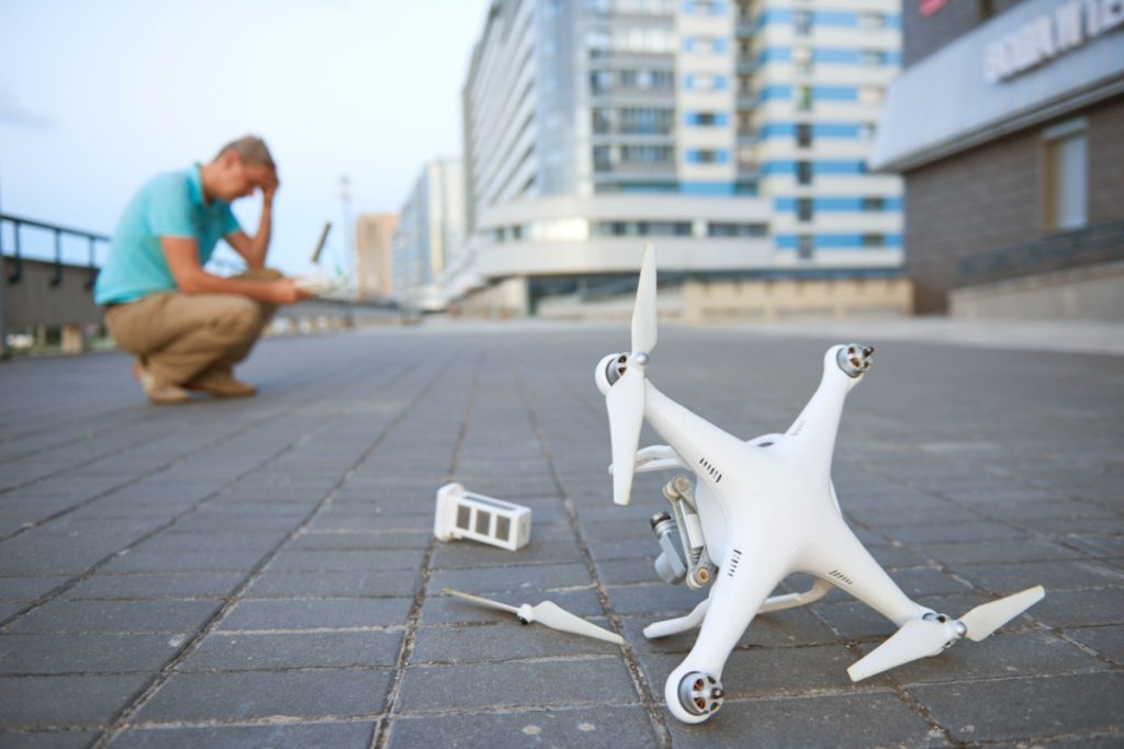 Drone crashed damaged, with man in the back frustrated in city.